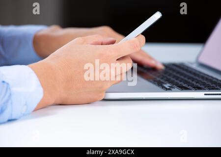 Vue latérale des mains d'une femme à l'aide d'un téléphone intelligent et d'un ordinateur portable Banque D'Images