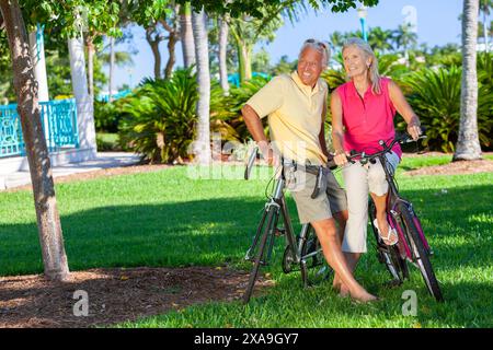 Heureux homme senior et femme retraité couple ensemble souriant à vélo sur des vélos dans un parc Banque D'Images