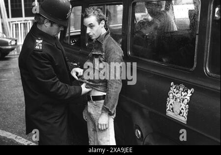 La police arrête un Punk Rocker sur Kings Road, Chelsea. La loi sus permettait à la police d'arrêter et de fouiller n'importe quelle « personne suspécieuse » ou « personne suspectée » n'importe où et n'importe quand. Le punk aux cheveux pointus est Mick Vessel qui figure dans le film de Wolfgang Büld, « Punk in London ». Kings Road, Chelsea, Londres, Angleterre 1977 1970s UK HOMER SYKES Banque D'Images