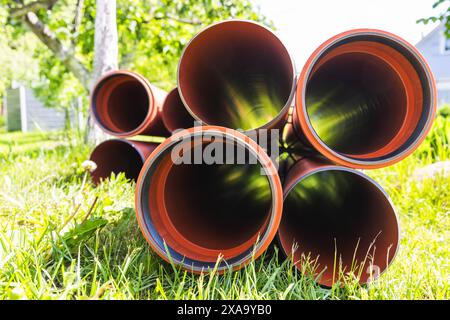 Les tuyaux pour les égouts externes reposent sur l'herbe par une journée ensoleillée, vue en perspective, éléments du système d'égouts souterrain extérieur Banque D'Images