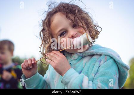 fille de 5 ans mangeant des guimauves grillées pendant le voyage de camping Banque D'Images