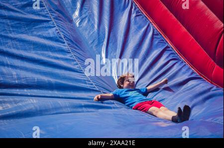 garçon de 6 ans glissant vers le bas toboggan de château gonflable Banque D'Images