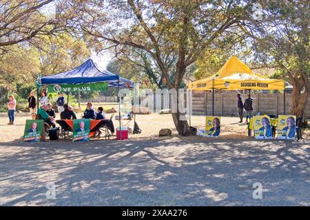 Vanderbijlpark, Gauteng, Afrique du Sud - 29 mai 2024 : deux kiosques de partis de campagne au bureau de vote avec des gens qui demandent à voter à l'arrière-plan Banque D'Images