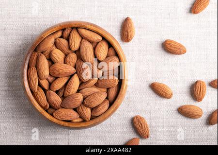 Amandes dans un bol en bois sur tissu de lin. Noix décortiquées, crues, entières et séchées, drupes botaniques, graines et fruits de Prunus dulcis. Banque D'Images