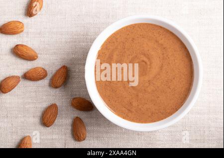 Faire dorer le beurre d'amande dans un bol blanc sur tissu de lin. Pâte alimentaire lisse fabriquée à partir de la mouture des amandes en beurre de noix. Purée de noix de Prunus dulcis. Banque D'Images