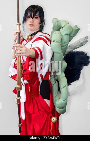 Une cosplayer féminine dans une tenue blanche et rouge et une cloche autour de son cou posant avec un arc et une flèche Banque D'Images