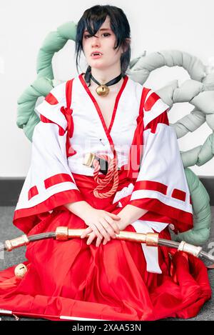 Une cosplayer féminine dans une tenue blanche et rouge et une cloche autour de son cou posant avec un arc et une flèche Banque D'Images