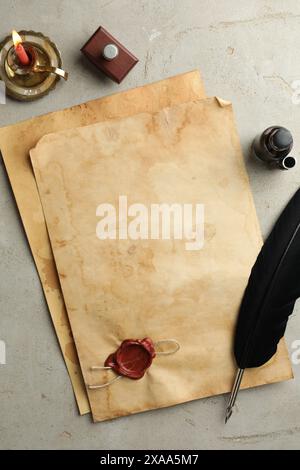 Feuille de vieux papier parchemin avec tampon de cire, plume noire, encrier et bougie sur table grise, pose à plat Banque D'Images