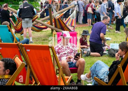 Personnes visiteurs homme portant chapeau de paille rose livre de lecture assis dans des transats au site du festival Hay 2024 Hay-on-Wye Wales Royaume-Uni Grande-Bretagne KATHY DEWITT Banque D'Images