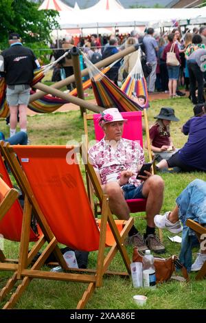 Personnes visiteurs homme portant chapeau de paille rose livre de lecture assis dans des transats au site du festival Hay 2024 Hay-on-Wye Wales Royaume-Uni Grande-Bretagne KATHY DEWITT Banque D'Images