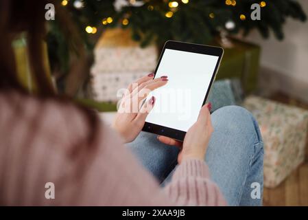 Maquette, tablette dans les mains d'une fille. Dans le contexte du nouvel an et de l'arbre de Noël. Concept de shopping en ligne, réductions ou com en ligne Banque D'Images