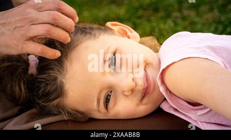 La petite fille caucasienne sourit sur les genoux de sa mère par une journée ensoleillée dans le parc. Un moment intime plein d'amour et de connexion familiale Banque D'Images