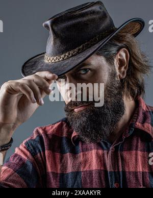 Beau jeune homme ajustant son chapeau de cow-boy. Des cowboys en chapeau. Beau macho barbu. Homme non rasé cow-boys. Cow-boy américain. Chapeau de cow-boy en cuir Banque D'Images