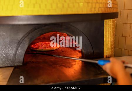 Pizzaiolo tout en vérifiant une pizza en cours de cuisson dans le four à bois avec sa pelle à four. Concept de pizza. Préparation de pizzas italiennes traditionnelles. Pelle pour pi Banque D'Images