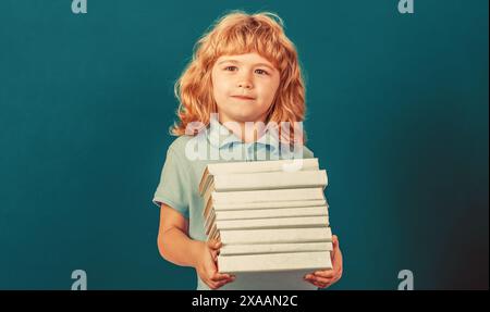 Heureux écolier avec des livres près du tableau noir. Retour à l'école. Écolier en classe. Enfant tenant pile de livres avec tableau de mortier sur tableau noir Banque D'Images