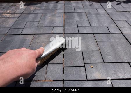 Homme brossant le patio de carreaux de terrasse composite nouvellement posés avec une brosse à main. Concept d'améliorations de la maison de jardin. Banque D'Images