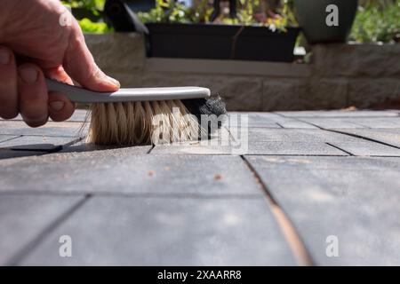 Homme brossant le patio de carreaux de terrasse composite nouvellement posés avec une brosse à main. Concept d'améliorations de la maison de jardin. Banque D'Images