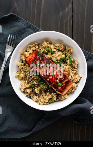 Saumon poêlé avec risotto aux champignons dans un bol à pâtes : filet de saumon mariné sur un lit de risotto aux champignons avec échalotes et garniture de graines de sésame Banque D'Images