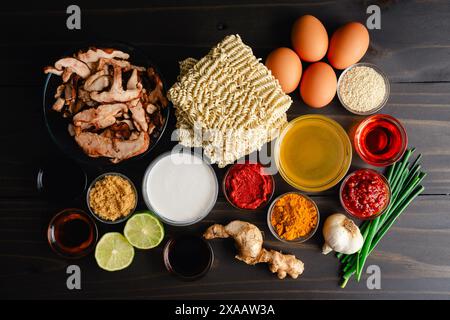 Ingrédients ramen au curry de noix de coco épicé sur une table en bois : nouilles ramen instantanées, champignons shiitake, pâte de curry et autres ingrédients Banque D'Images