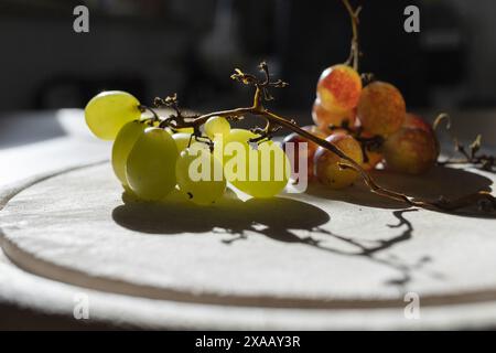 gros plan rétroéclairé de raisins verts et rouges sur une planche à découper en bois Banque D'Images