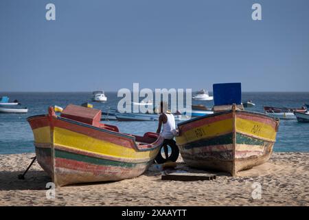 Homme local se reposant entre des bateaux de pêche colorés sur la plage de Praia de Santa Maria, Santa Maria, Sal, îles du Cap Vert, Atlantique, Afrique Banque D'Images