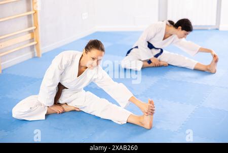 Deux femmes en kimonos faisant des étirements avant l'entraînement de karaté ou de judo Banque D'Images