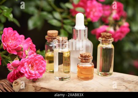 Plusieurs bouteilles d'huile essentielle d'aromathérapie avec des fleurs de rose rose à l'extérieur dans un jardin Banque D'Images