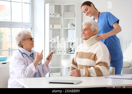 Médecin senior et infirmière posant un collier cervical sur un homme mature en clinique Banque D'Images