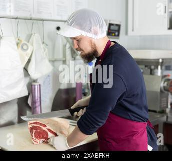 Boucher coupant le bœuf avec un grand couteau dans la salle de transformation du supermarché Banque D'Images