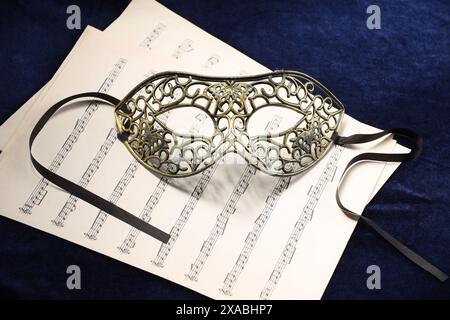 Masque facial élégant et feuilles de musique sur tissu bleu. Représentation théâtrale Banque D'Images