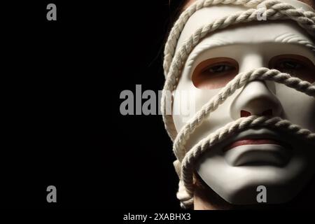 Représentation théâtrale. Homme avec masque en plastique et corde de chanvre sur fond noir, espace pour le texte Banque D'Images