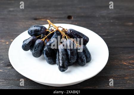 Raisins à doigt de sorcière violets ou raisin saphir sur assiette blanche Banque D'Images