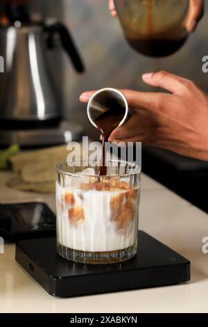 Barista à main masculin versant du chocolat espresso au café noir à l'aide d'une tasse à mesurer dans le verre avec du lait frais et de la glace Banque D'Images