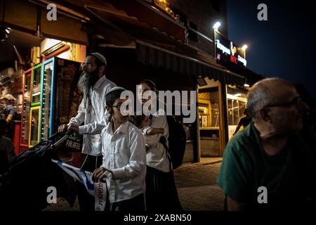 Une famille religieuse israélienne passe devant un magasin palestinien près de la porte de Damas à Jérusalem, jeudi 5 juin 2024. Des dizaines de milliers de jeunes religieux et sionistes ont défilé à travers la capitale en brandissant des drapeaux de l'étoile de David pour entrer dans la vieille ville de Jérusalem par le quartier musulman, dans le cadre d'une marche controversée du drapeau, marquant la réunification de la ville pendant la guerre des six jours et IsraelÕs la prise du Mont du Temple et du mur occidental, JudaismÕs lieux les plus saints. Photo par Eyal Warshavsky. Banque D'Images