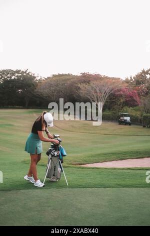 Une femme joue au golf professionnellement. Elle se tient à côté du sac et choisit un club. Banque D'Images