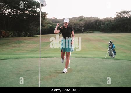 Une femme golfeuse professionnelle en jupe de sport et casquette frappe le trou avec la balle. Banque D'Images