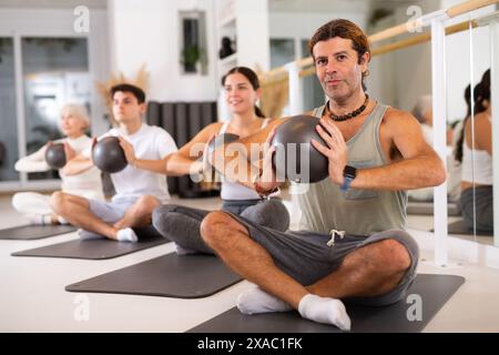 Homme d'âge moyen pratiquant des pilates avec ballon sur tapis gris dans la salle de gym Banque D'Images