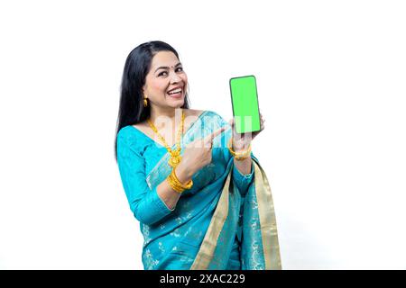 Heureuse jeune femme indienne portant saree bleu et bijoux en or tenant le téléphone intelligent avec affichage vierge pour mettre la publicité sur fond blanc Banque D'Images