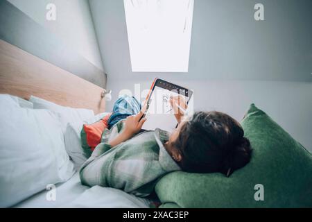 Dans le confort tranquille de sa chambre, une fille utilise sa tablette pour dessiner, trouvant réconfort et évasion thérapeutique à travers ses dessins numériques Banque D'Images