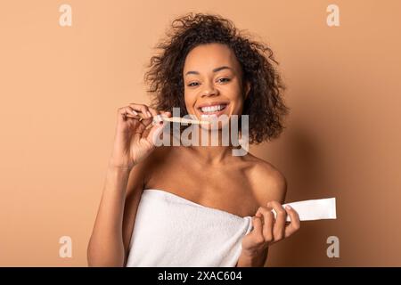 Jeune femme aux cheveux bouclés se brossant les dents avec une brosse à dents en bambou Banque D'Images