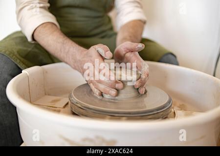 Le potier masculin adulte s'engage dans l'art de sculpter un plat en céramique à l'aide d'une roue de potier, mettant en valeur l'habileté et la précision. Banque D'Images