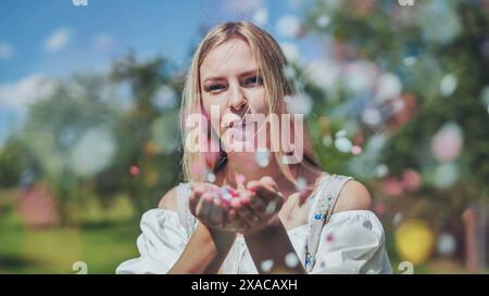 Une fille souffle des confettis en papier multicolores de ses mains. Banque D'Images