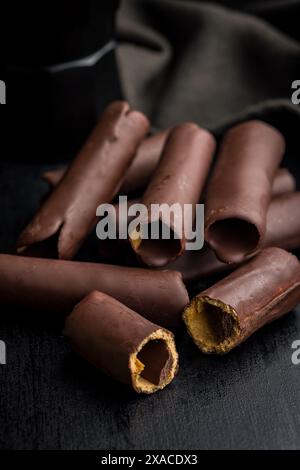 Un gros plan de gaufrettes recouvertes de chocolat couchées sur une table sombre. Les plaquettes sont disposées en pile. L'image est focalisée sur la texture et le détail o Banque D'Images