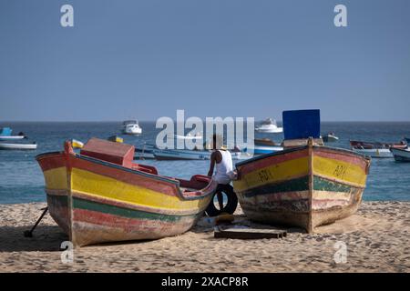 Homme local se reposant entre des bateaux de pêche colorés sur la plage de Praia de Santa Maria, Santa Maria, Sal, îles du Cap Vert, Atlantique, Afrique Copyright : Ala Banque D'Images