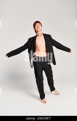 Un jeune homme élégant en costume frappe une pose confiante dans un studio avec un fond gris. Banque D'Images