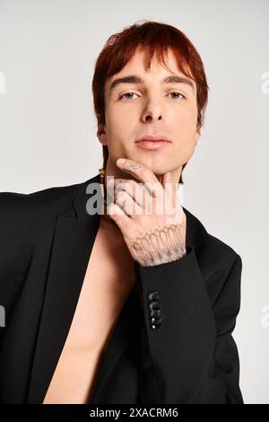 Un jeune homme élégant dans un costume noir frappant une pose confiante sur un fond de studio gris. Banque D'Images