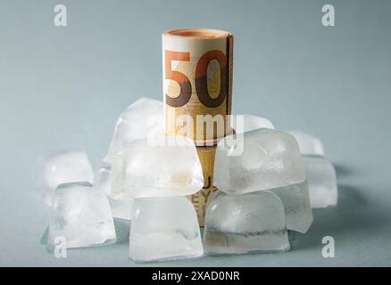 Concept de gel des fonds. Euro Money roll à l'intérieur des glaçons sur fond bleu de studio. Copier l'espace. Banque D'Images