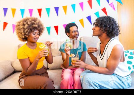 Amis multiethniques buvant des cocktails faisant la fête à la maison assis sur le canapé discutant Banque D'Images