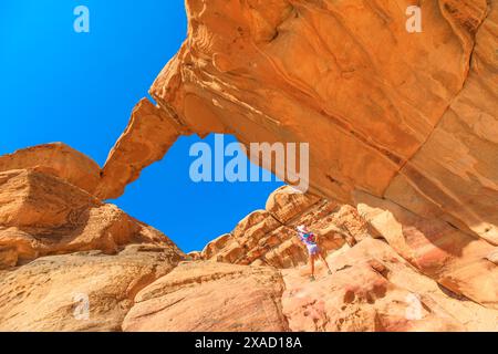 Seule femme touristique est assise contemplativement sous la magnifique arche rocheuse Um Fruth dans la vaste étendue du désert du Wadi Rum en Jordanie, mettant en valeur le Banque D'Images