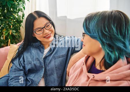 Mère asiatique et fille adolescente s'engagent dans une conversation sincère sur un canapé confortable à la maison, créant une atmosphère chaleureuse et aimante. Banque D'Images